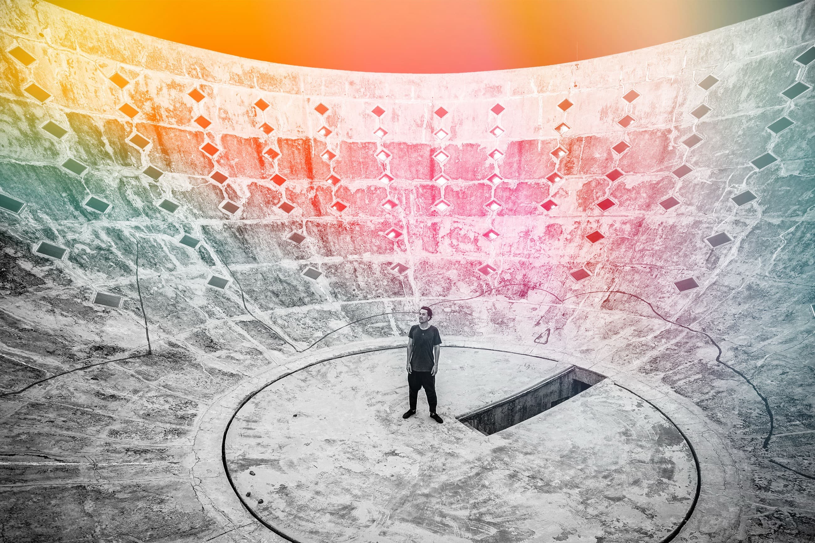 Nico Stojan standing alone at the centre of a vast concrete amphitheatre under a sweep of dawn-coloured light